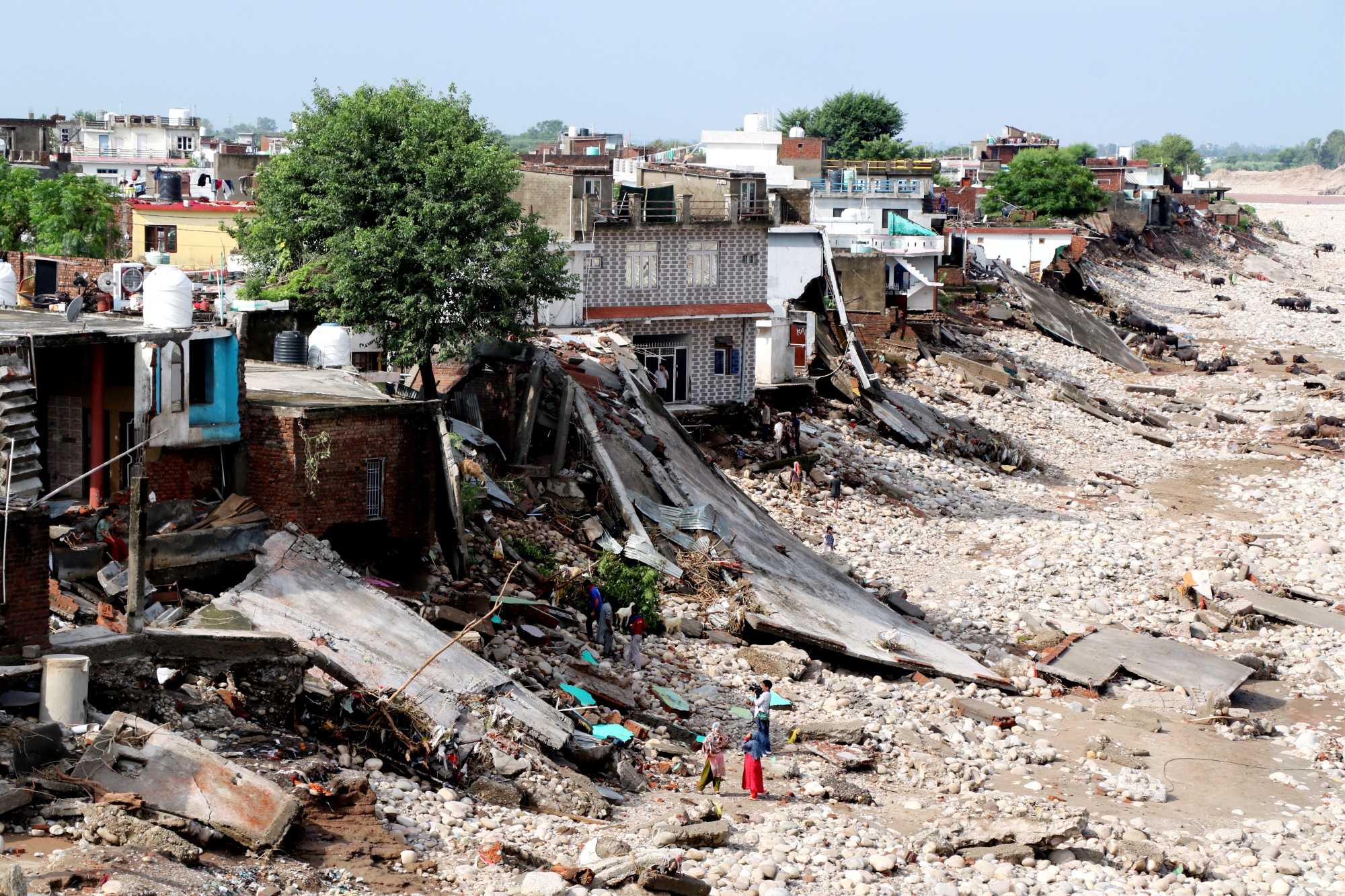 जम्मू में भारी बारिश के कारण तवी नदी के उफान पर आने के एक दिन बाद लोग नदी के किनारे क्षतिग्रस्त घरों के पास खड़े हैं.